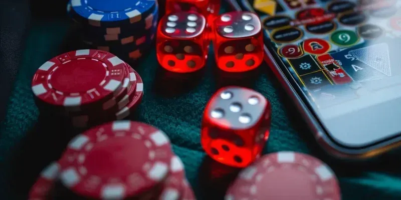 Fichas de cassino empilhadas e dados vermelhos ao lado de um celular